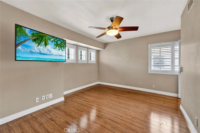 an empty room with wooden floor fan and windows