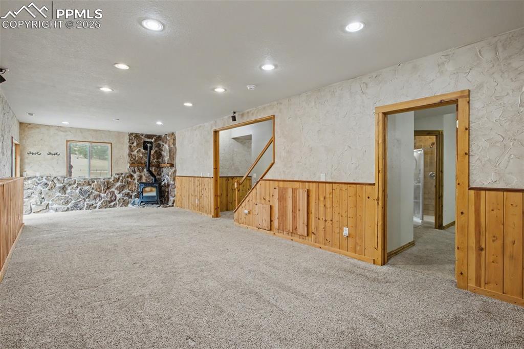 4944 Antelope Trail Elbert, CO 80106 - Photo 23 of 49 Empty room featuring a wainscoted wall, a wood stove, carpet, wood walls, and recessed lighting