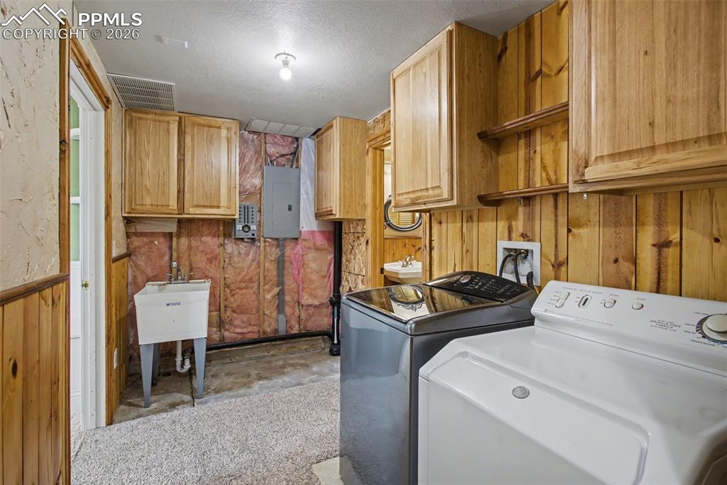 4944 Antelope Trail Elbert, CO 80106 - Photo 28 of 49 Laundry area featuring wood walls, a textured ceiling, concrete flooring, electric panel, and washer and clothes dryer