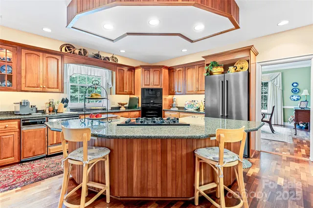 a kitchen with stainless steel appliances granite countertop a stove top oven a refrigerator a sink and dishwasher with wooden floor