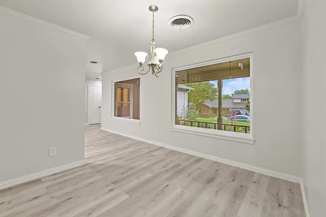 an empty room with wooden floor chandelier and windows