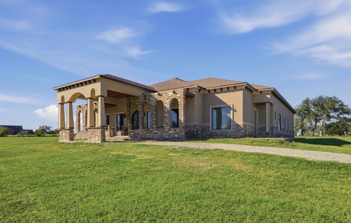 7348 Love Road Fulshear, TX 77441 - Photo 2 of 48 Stunning stone-accented home with elegant arches and a welcoming glow, set against a picturesque sunset backdrop..