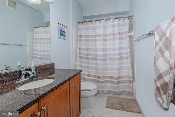 a bathroom with a granite countertop sink a toilet a mirror and shower curtain