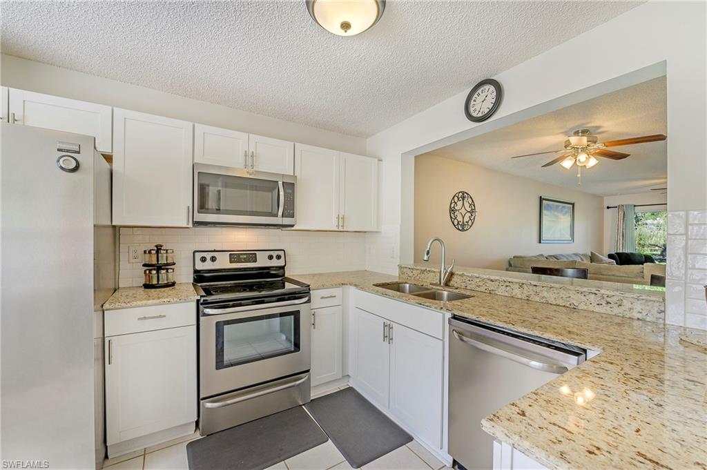 5737 Whitaker Road, Unit C103 Naples, FL 34112 - Photo 7 of 22 a kitchen with granite countertop a sink stainless steel appliances and white cabinets