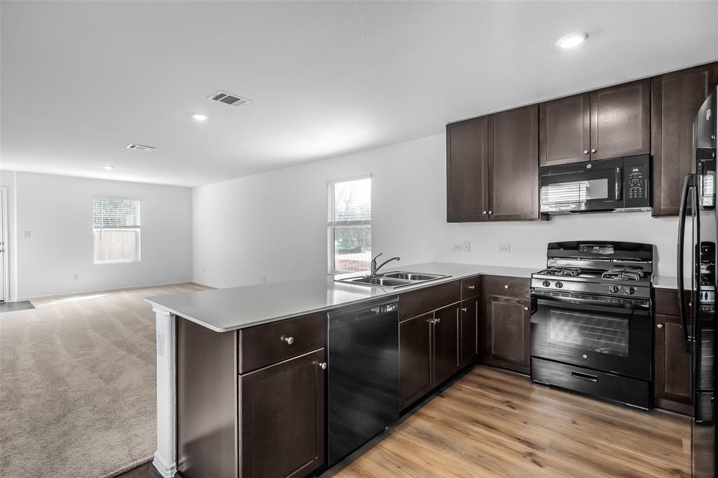 61 Trinity Circle Lockhart, TX 78644 - Photo 2 of 14 Open-concept kitchen featuring dark wood cabinetry, light-toned countertops, and a black appliance suite with a gas range