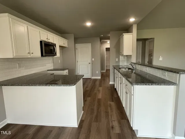 a kitchen with granite countertop a sink a stove top oven a granite counter space and cabinets