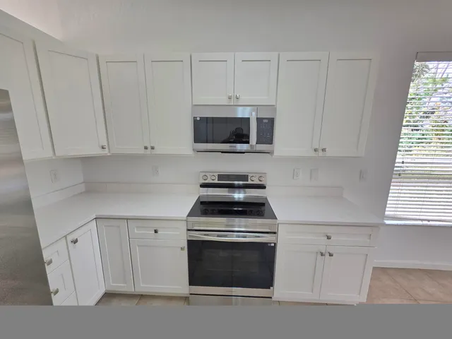 a kitchen with granite countertop white cabinets white appliances a sink and a window