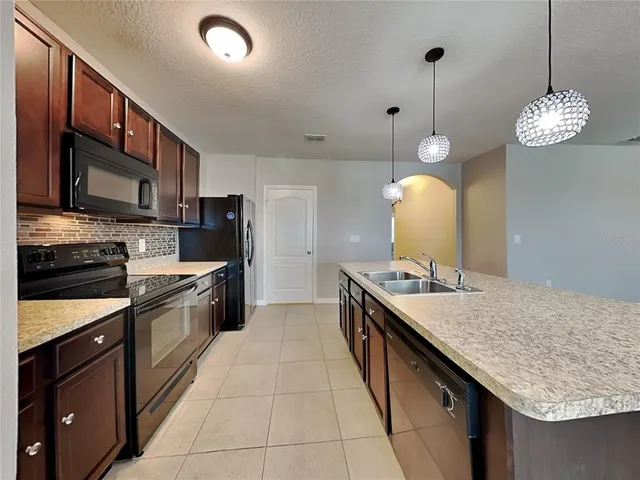 a kitchen with kitchen island granite countertop stainless steel appliances a stove a sink cabinets a refrigerator and a stove