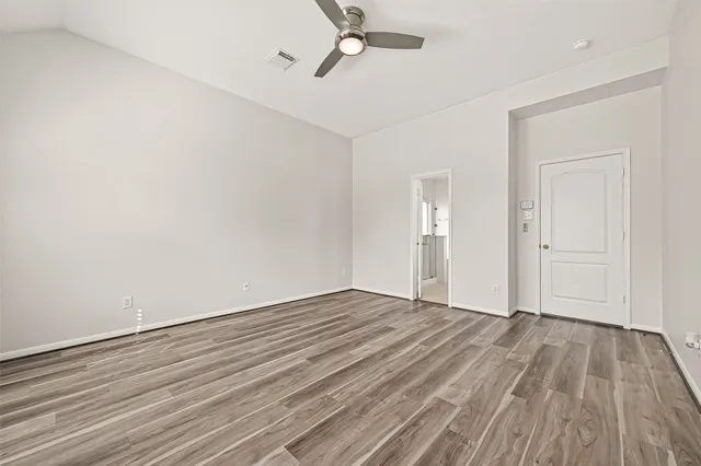 an empty room with wooden floor ceiling fan and windows
