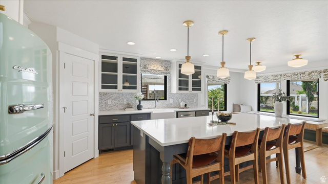2038 East Ranch Road Eagle Mountain, UT 84005 - Photo 11 of 66 Spacious kitchen featuring a large central island with seating, a patterned tile backsplash, white shaker-style upper cabinetry, dark lower cabinetry, and wood-finish flooring