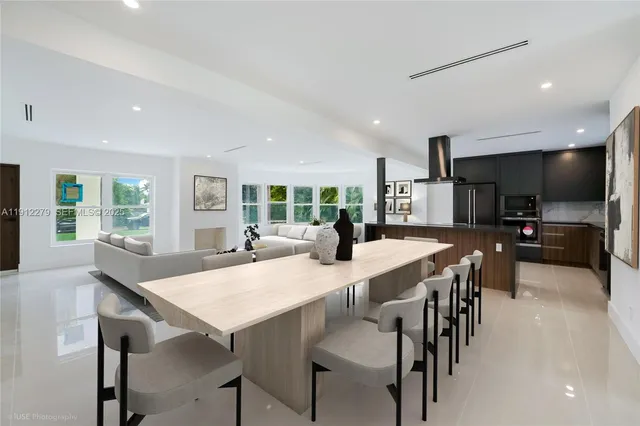 a kitchen with stainless steel appliances kitchen island granite countertop a dining table chairs and a refrigerator