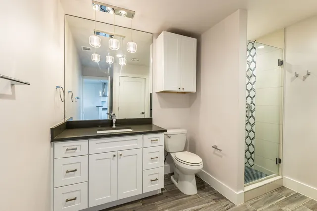 a bathroom with a granite countertop sink a toilet a mirror and shower
