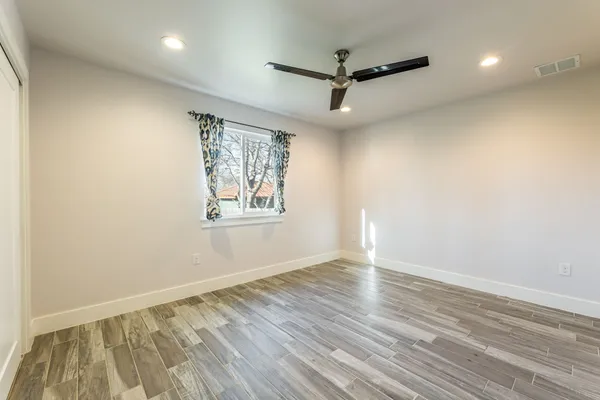 an empty room with wooden floor ceiling fan and windows