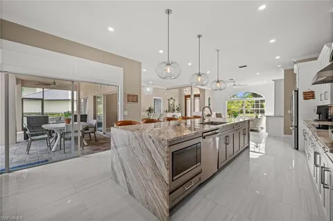 a kitchen with stainless steel appliances kitchen island granite countertop a stove a sink a oven and a dining table with white cabinets