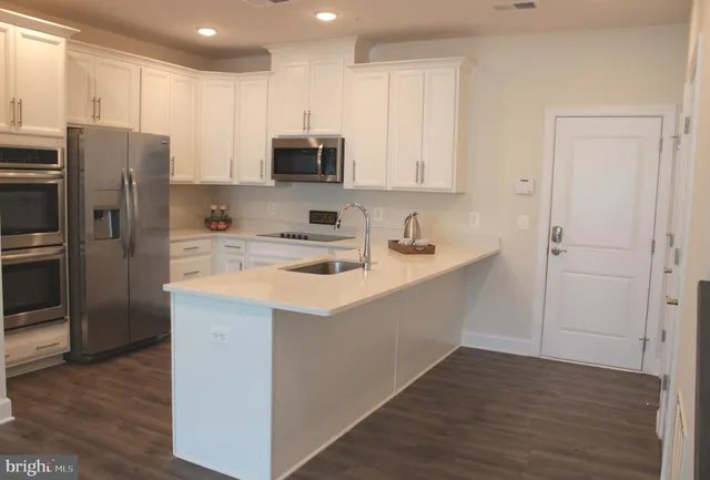 a kitchen with stainless steel appliances a sink a stove a refrigerator cabinets and a wooden floor