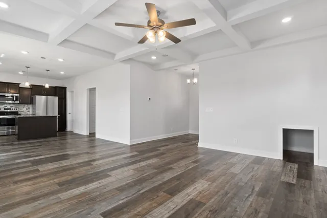 an empty room with wooden floor a ceiling fan and kitchen view