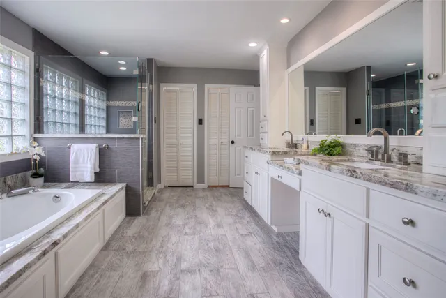 a large white bathroom with a granite countertop double vanity sink a mirror and a bathtub