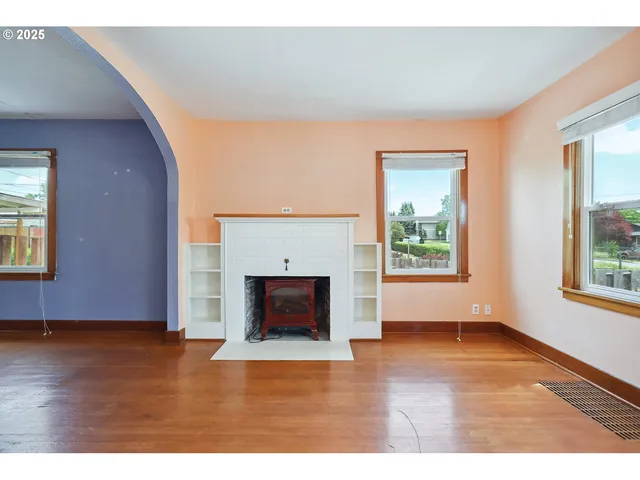 a view of an empty room with wooden floor fireplace and a window