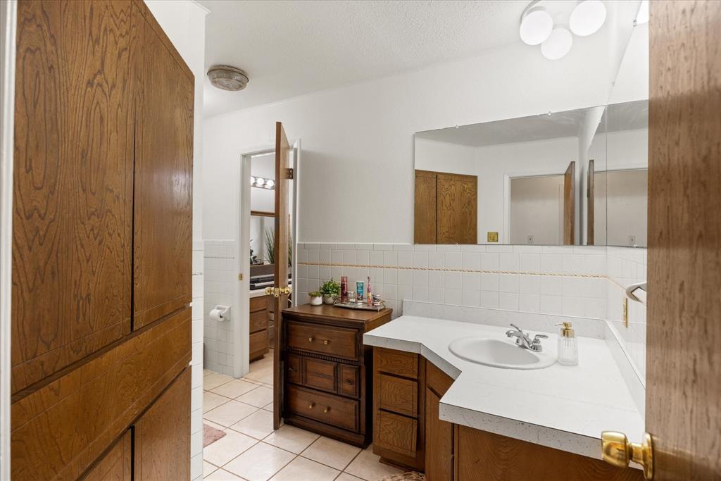 4210 Waples Road Granbury, TX 76049 - Photo 33 of 37 Bathroom featuring a white countertop with integrated sink, wood-finish cabinetry, a large wall-mounted mirror, white square tile wainscoting, and a built-in wood-finish linen cabinet