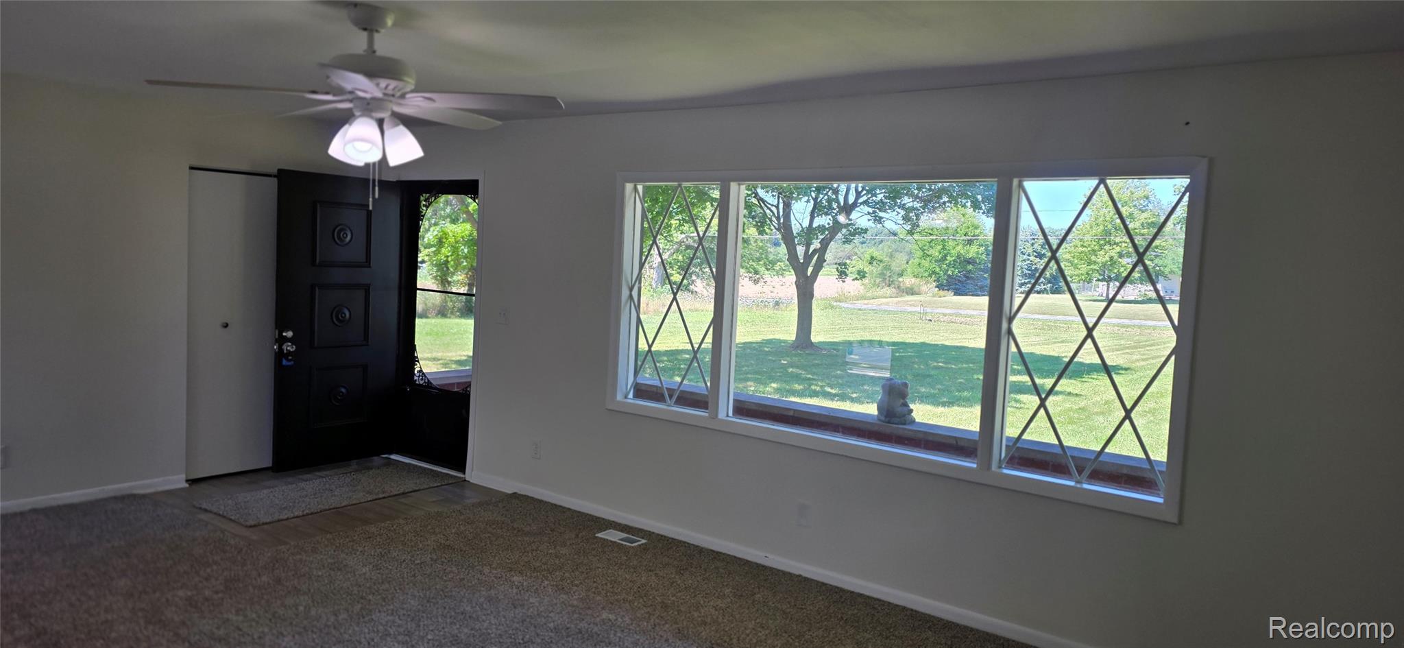 4363 West Dodge Road Clio, MI 48420 - Photo 4 of 52 Spacious room featuring broad picture windows with diamond-patterned grilles, a black front door, a ceiling fan with integrated lighting, and neutral-toned carpeting