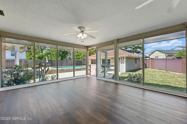 a view of an empty room with wooden floor and a ceiling fan