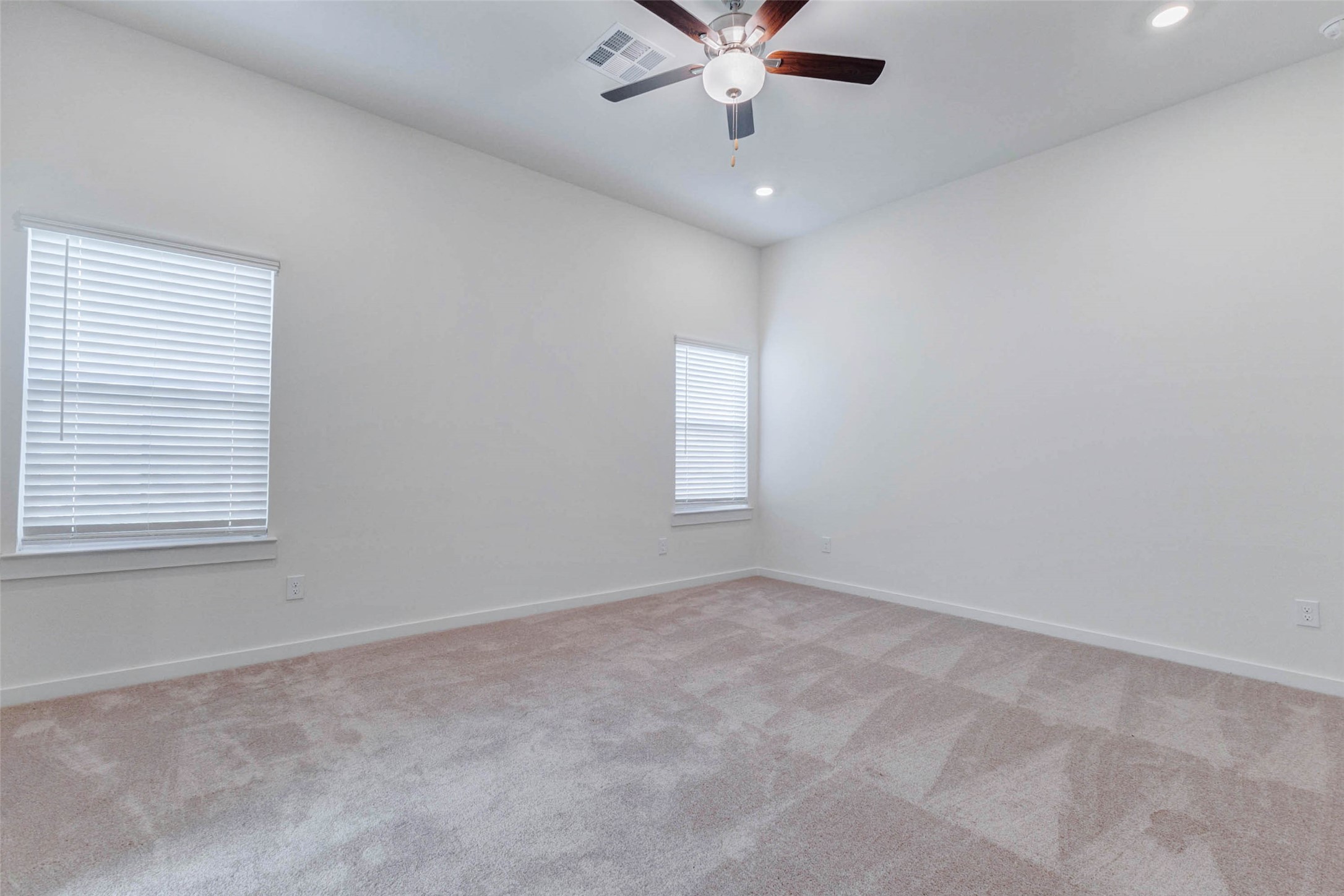 6467 Escondido Drive Rosharon, TX 77583 - Photo 16 of 32 Spacious primary bedroom with soft carpet, high ceilings, ceiling fan, recessed lighting, and two windows bringing in natural light. The neutral walls and generous floor space create a calm, comfortable retreat with plenty of room for a full bedroom setup, sitting area, or personalized décor.