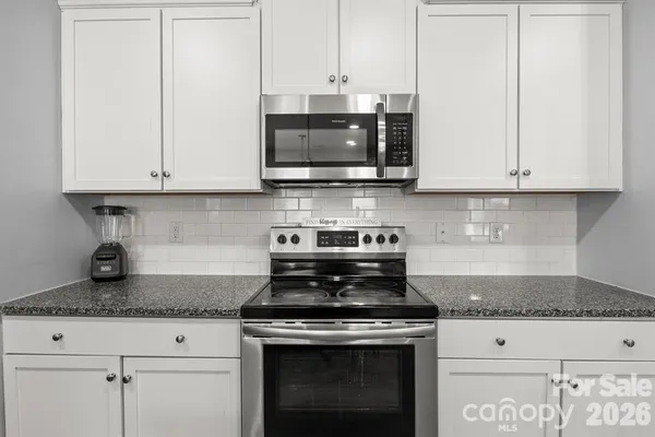 a kitchen with stainless steel appliances granite countertop white cabinets and a stove a sink