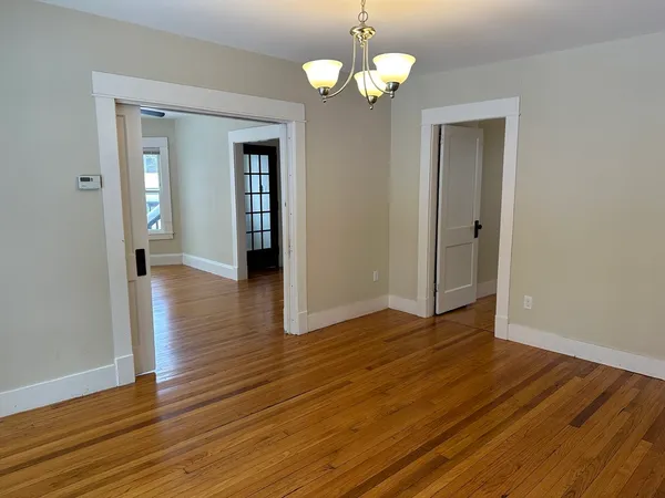 a view of an empty room with wooden floor and a chandelier