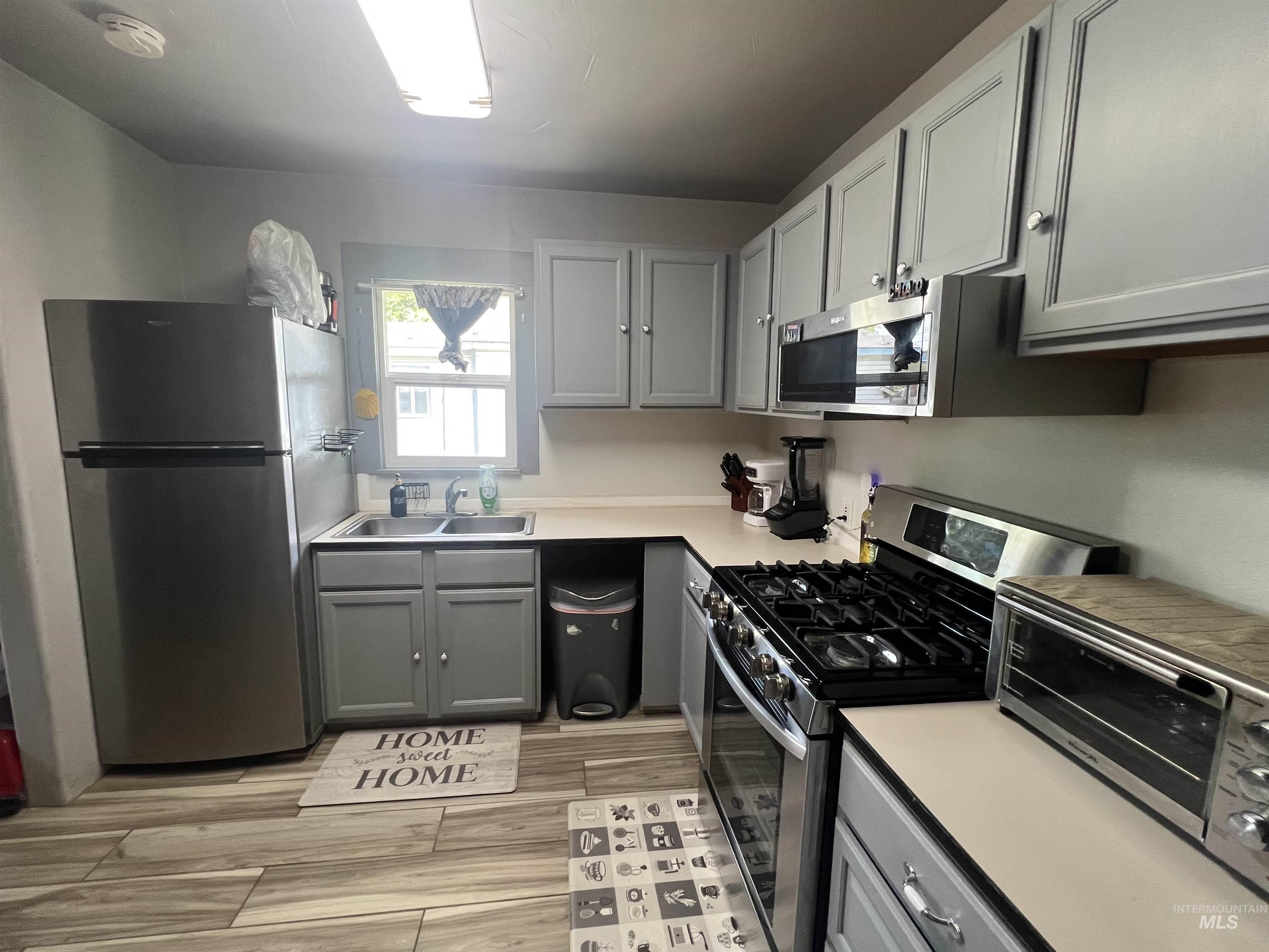 121 North 1st Street Nyssa, OR 97913 - Photo 6 of 20 Kitchen featuring wood-finish flooring, light-toned countertops, gray cabinetry with silver hardware, a double-basin sink, and stainless steel appliances