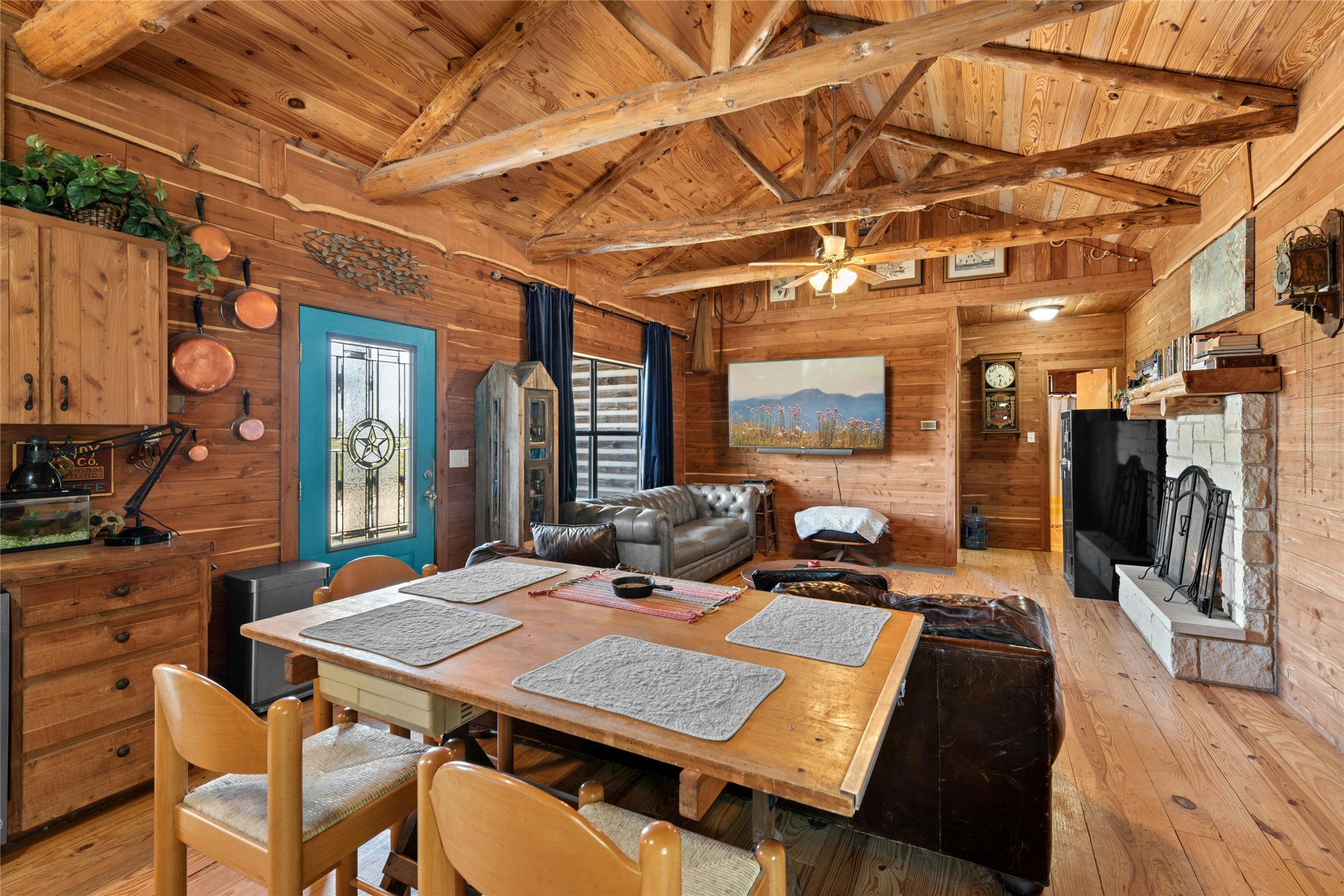 496 Middleton Road Spicewood, TX 78669 - Photo 14 of 40 Expansive living area featuring wood-finish walls and flooring, an exposed beam vaulted ceiling, a stone-clad fireplace with mantel, and a ceiling fan