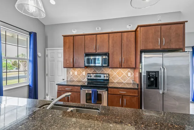 a kitchen with stainless steel appliances granite countertop a refrigerator a sink dishwasher a stove and a dining table with wooden floor