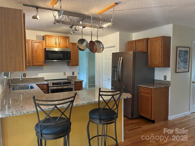 a kitchen with stainless steel appliances granite countertop a stove a refrigerator a sink a dining table and chairs with wooden floor