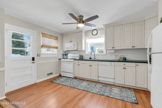 a kitchen with granite countertop white cabinets white appliances a sink and a window