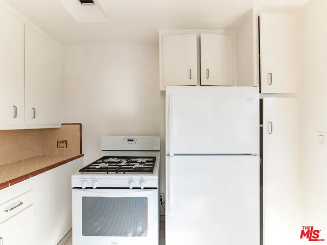 a kitchen with a stove a refrigerator and white cabinets