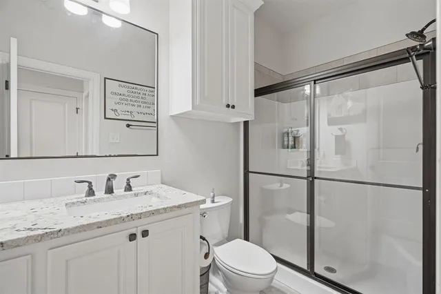 a bathroom with a granite countertop shower sink vanity and toilet