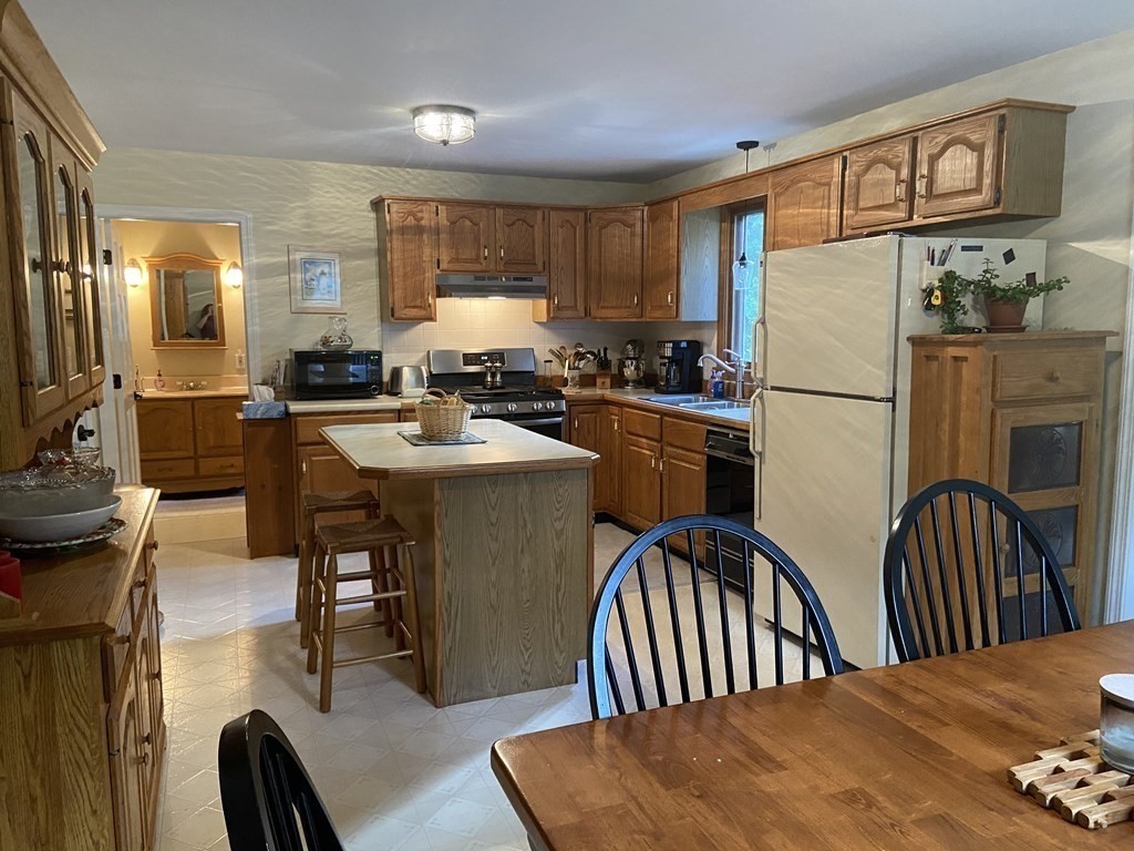 219 Forge Village Road Groton, MA 01450 - Photo 3 of 28 a kitchen with stainless steel appliances granite countertop a stove a refrigerator a sink a dining table and chairs with wooden floor