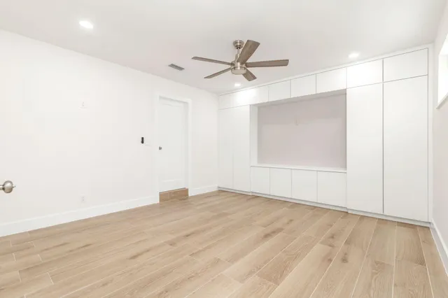 a view of an empty room with wooden floor and a ceiling fan