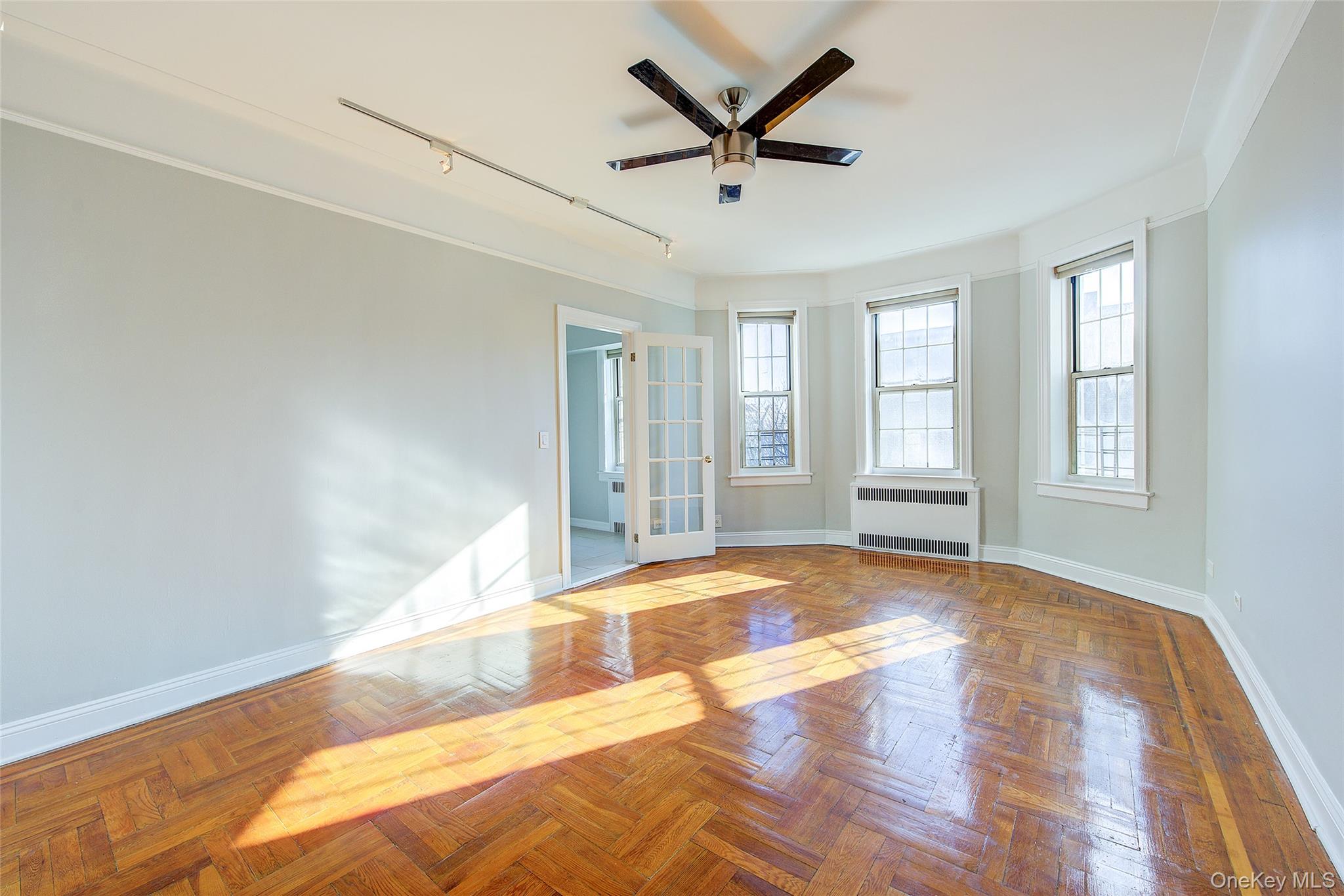 79-15 35th Avenue, Unit 5A Queens, NY 11372 - Photo 2 of 14 Unfurnished room with rail lighting, radiator heating unit, a ceiling fan, and healthy amount of natural light
