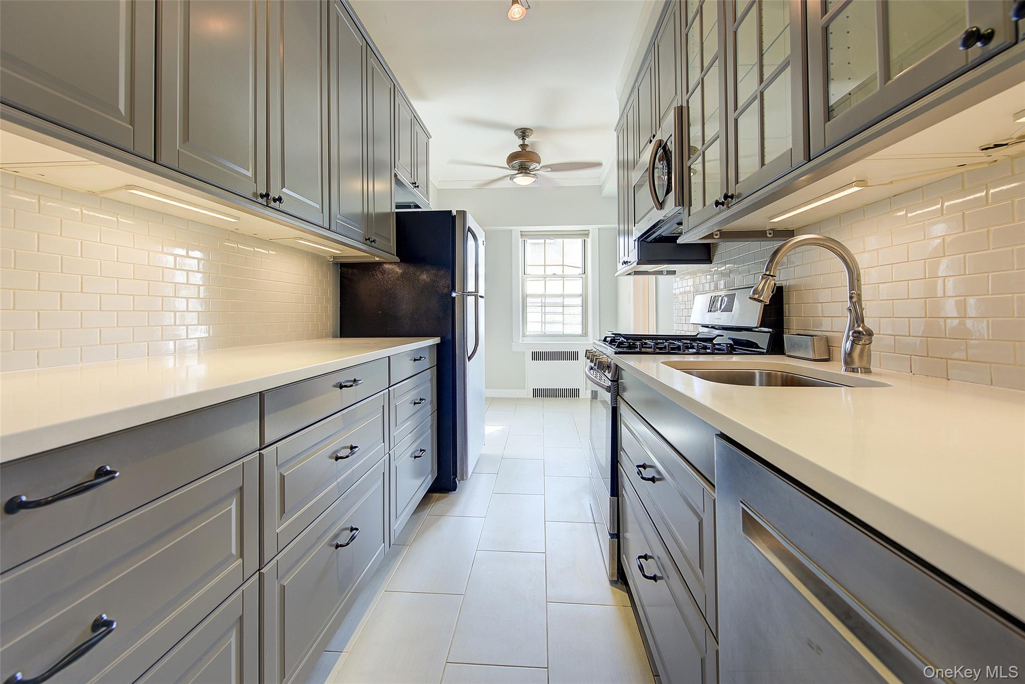 79-15 35th Avenue, Unit 5A Queens, NY 11372 - Photo 6 of 14 Kitchen with gray cabinetry, stainless steel appliances, tasteful backsplash, glass insert cabinets, and ceiling fan