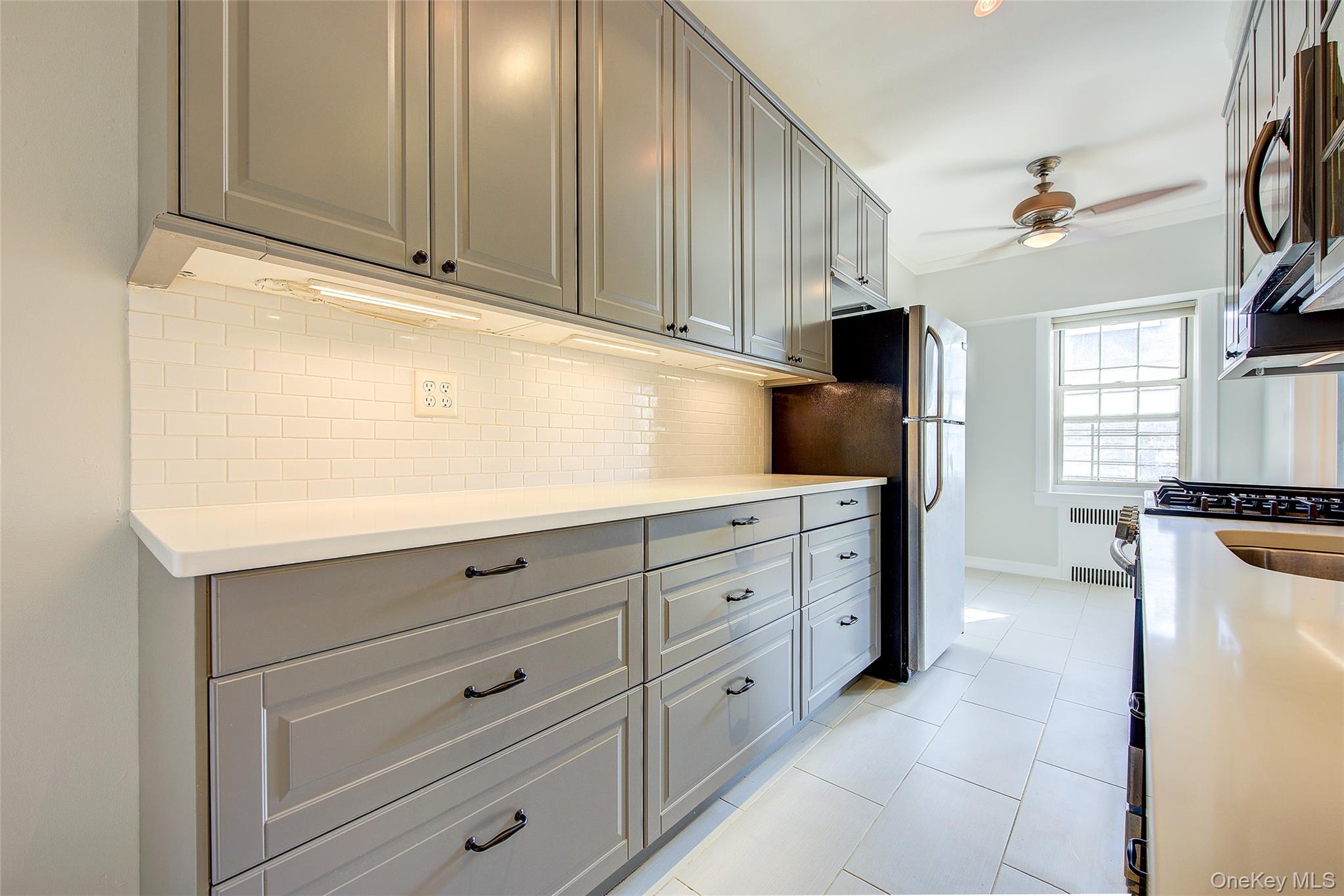79-15 35th Avenue, Unit 5A Queens, NY 11372 - Photo 7 of 14 Kitchen with gray cabinetry, stainless steel appliances, ceiling fan, decorative backsplash, and light tile patterned floors