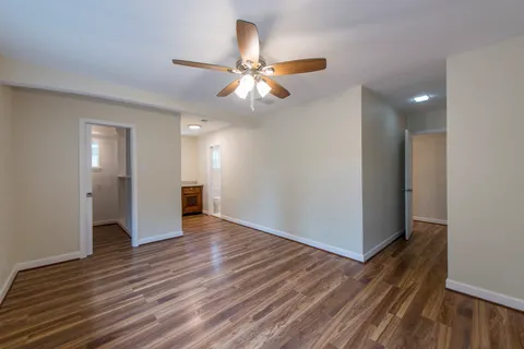 a view of an empty room with wooden floor and a ceiling fan