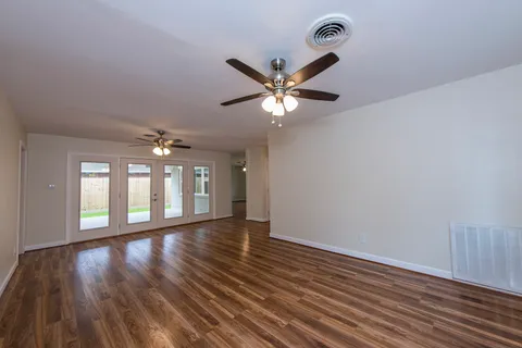 a view of an empty room with chandelier fan and wooden floor