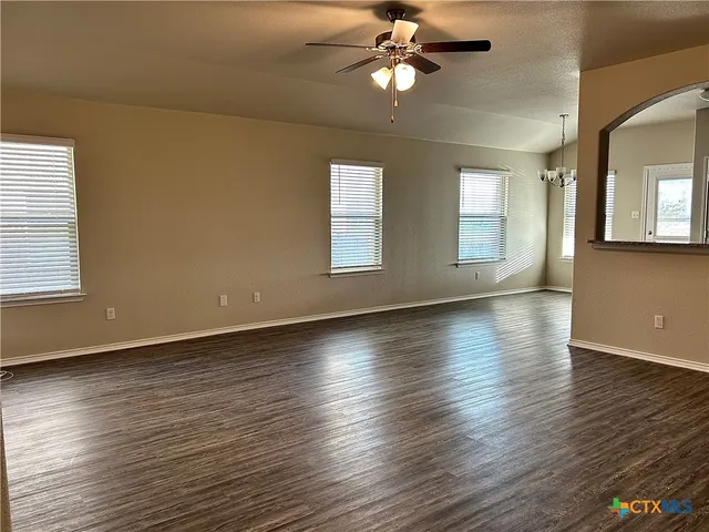 an empty room with wooden floor chandelier fan and windows