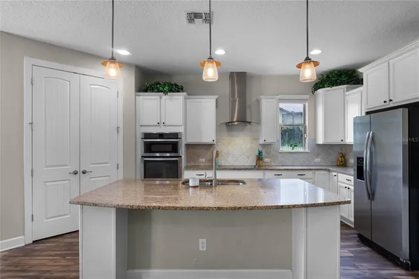 a kitchen with stainless steel appliances granite countertop a sink a refrigerator a stove a center island a refrigerator and a wooden floor