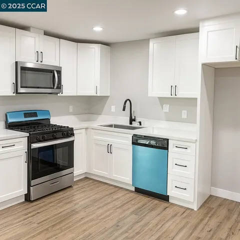 a kitchen with stainless steel appliances white cabinets a sink a stove a microwave and wooden floors