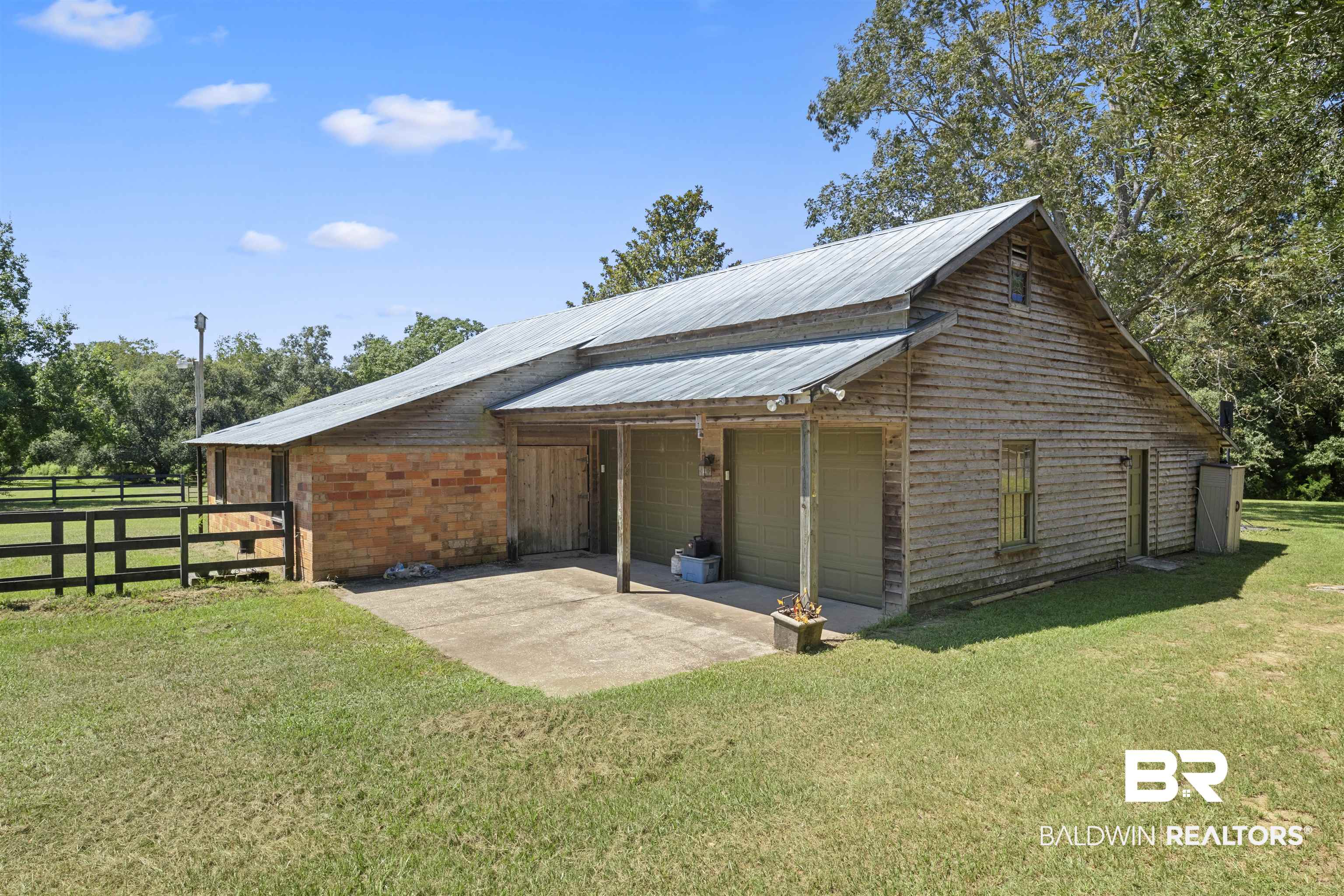 15100 Vasko Road Silverhill, AL 36576 - Photo 49 of 51 Two-car garage with workshop attached to two-story barn. Multiple doors open to allow for air and equipment to be moved in and out. Tractor parked on other side of barn adjacent to two stables.