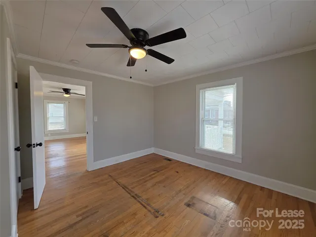 an empty room with wooden floor fan and windows