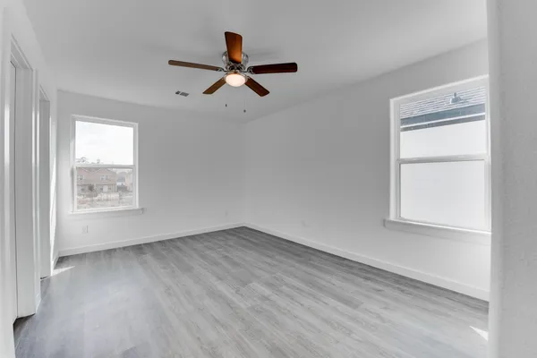 an empty room with wooden floor fan and windows