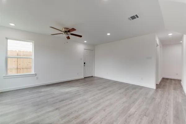 an empty room with wooden floor ceiling fan and window