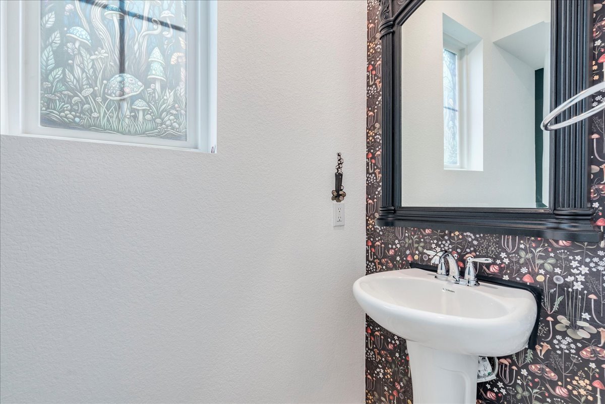 8008 Prairie Rye Drive Lago Vista, TX 78645 - Photo 27 of 40 Half bathroom downstairs with a Pedestal sink with chrome faucet, framed mirror, and decorative botanical-patterned wallpaper